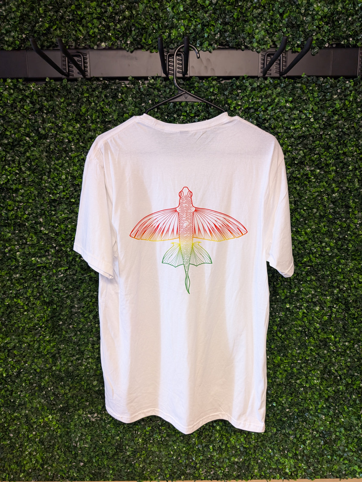 Back of white Puakea Rasta T-shirt with flying fish graphic in red, yellow, and green.