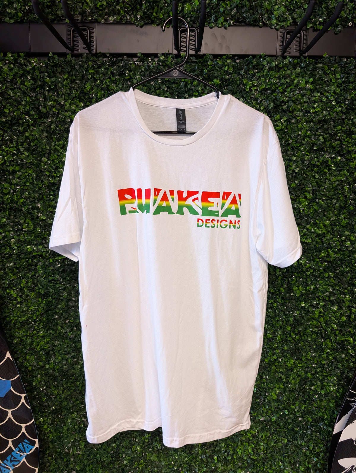 Front of white Puakea Rasta T-shirt with red, yellow, and green Puakea Designs lettering.